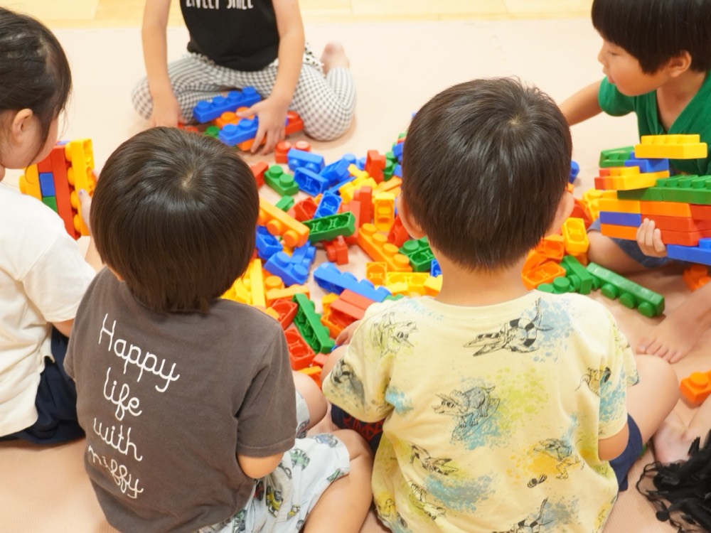 保育室の床に座り、色とりどりのブロックで一緒に遊ぶ子どもたち