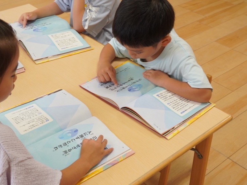 3・4・5歳児クラスの保育室で、子どもたちが机に向かって本を読んでいる様子