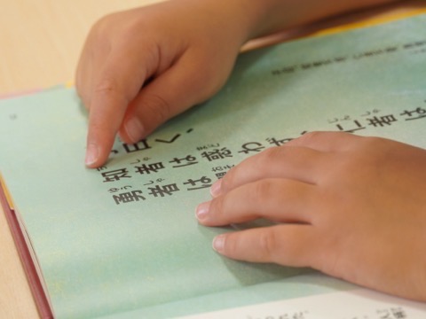 本の文字を指でなぞりながら読む子どもの手元