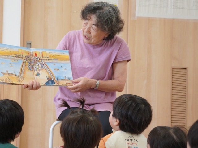 地域ボランティアの方が絵本を開いて見せ、子どもたちが座って聞いている様子