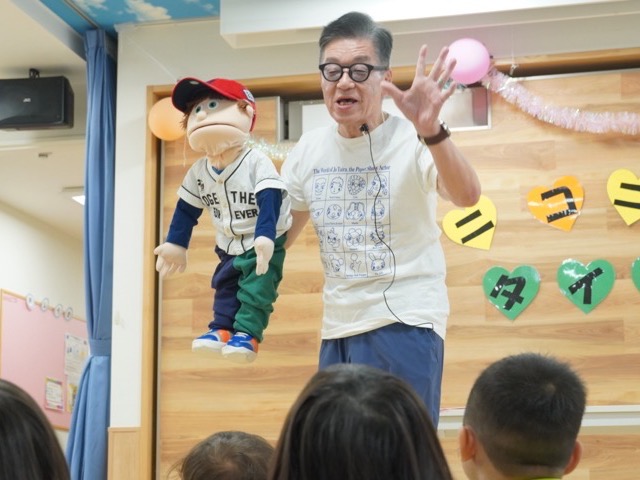 パペットを手にした地域ボランティアの方が、子どもたちの前で腹話術を披露している様子
